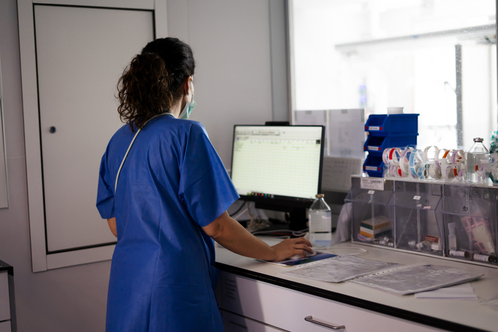 Nurse wearing surgical mask working on computer in hospital room